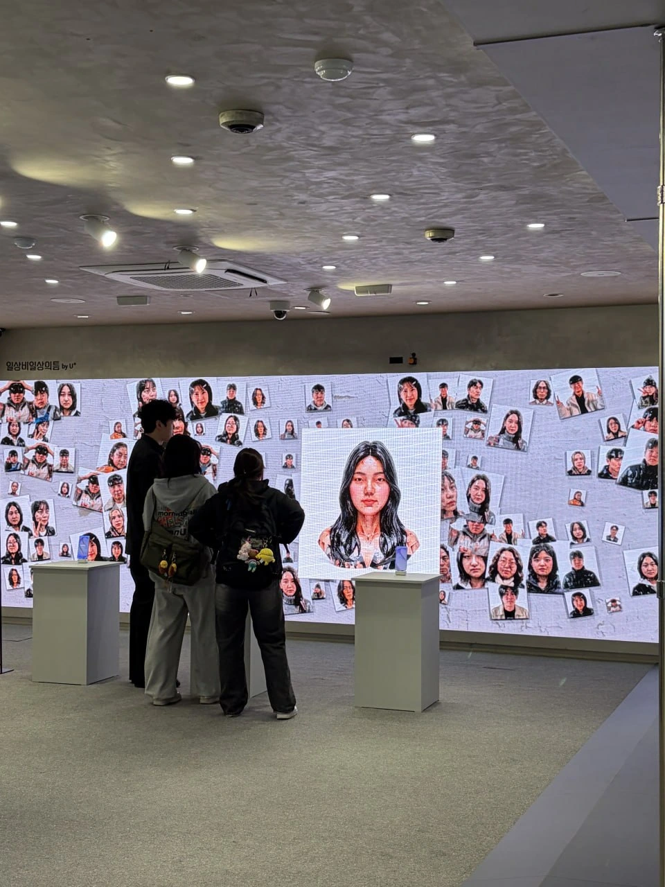 인물 사진 벽면 앞에서 콘텐츠를 살펴보는 관람객